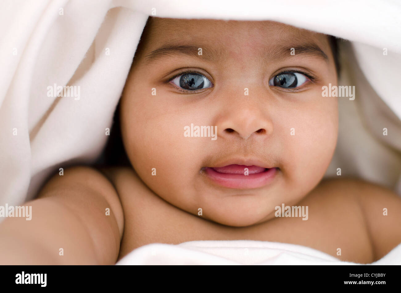 6 months old Indian baby girl smiling, lying on bed and covered by