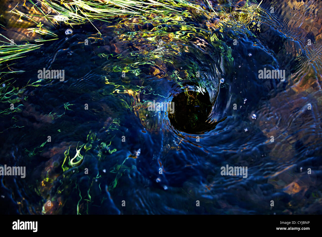 Blue water swirling down a hole in the ground Stock Photo - Alamy
