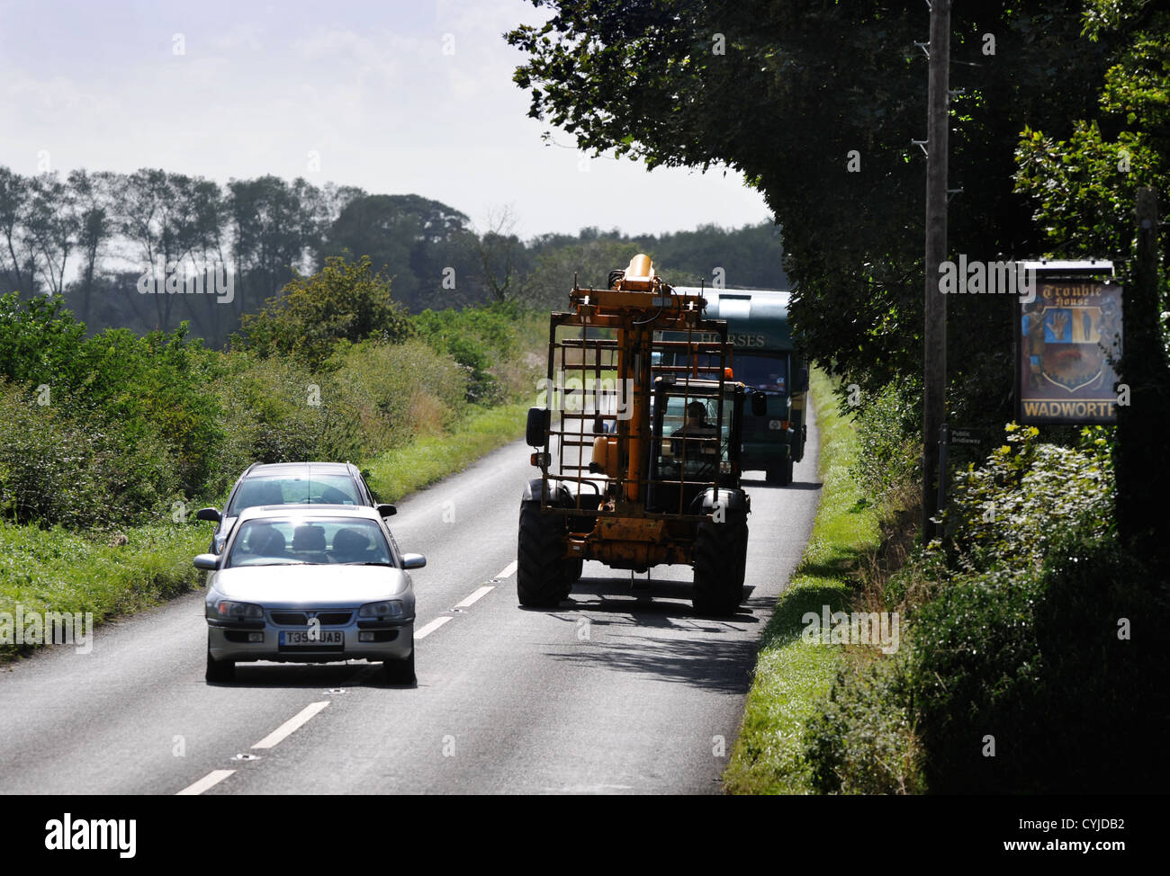 Cars overtaking an agricultural vehicle despite passing a pub entrance on a road in Gloucestershire UK Stock Photo