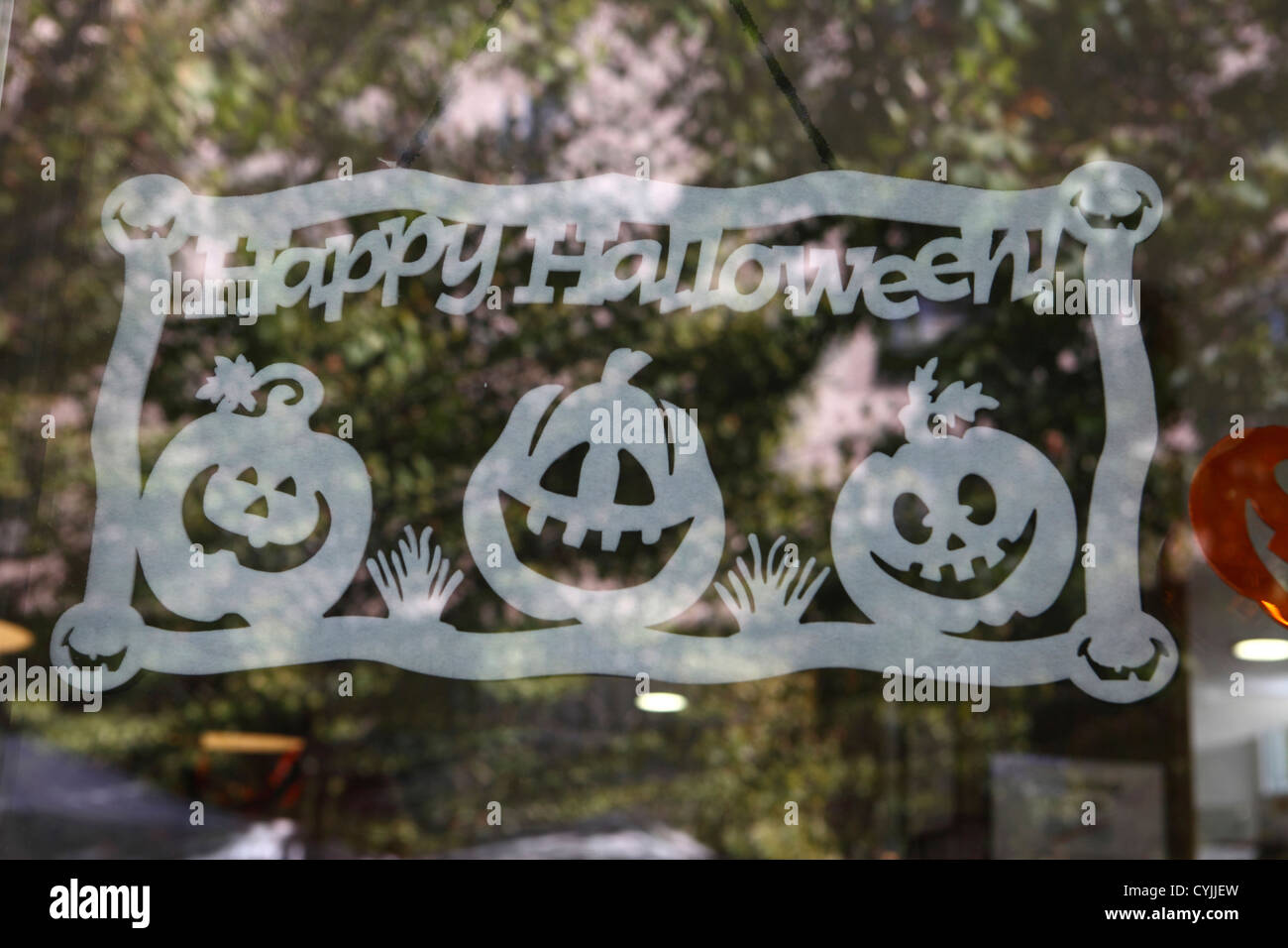 Cut-out stencil Happy Halloween sign in shop window with reflection of trees behind, Madrid, Spain Stock Photo