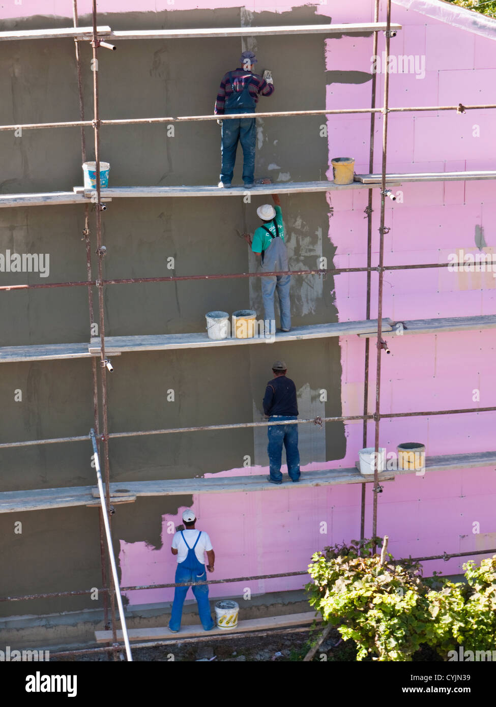 Workers applying render to an insulated building in Ohrid, Macedonia, where Health & Safety standards are behind those of the EU Stock Photo