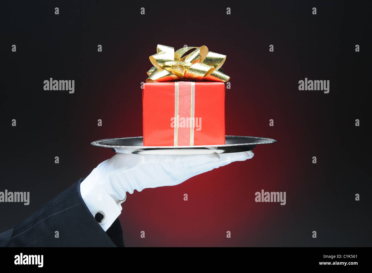 A butler wearing a tuxedo and white glove holding a tray with a wrapped present. Stock Photo