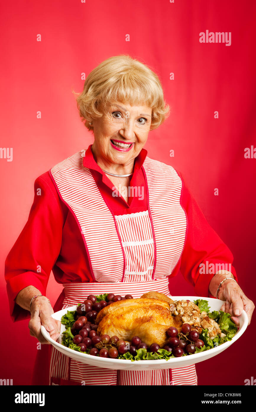 Sweet retro grandmother holding a Christmas or Thanksgiving holiday turkey dinner. Red background.  Stock Photo