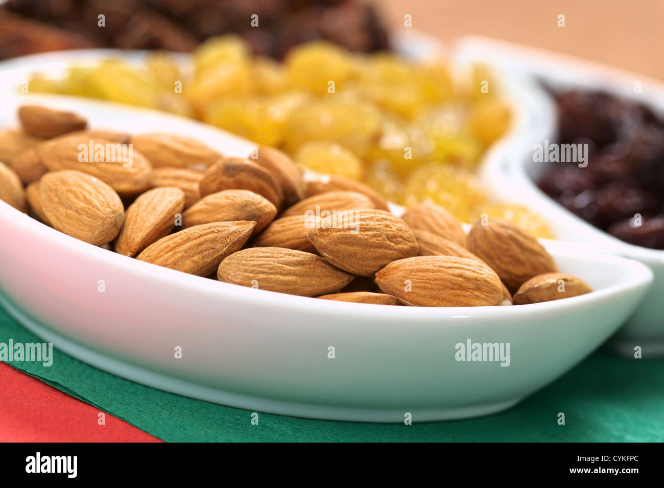 Almonds, sultanas and raisins in small bowls on red and green napkins (Selective Focus, Focus on the almonds in the front) Stock Photo
