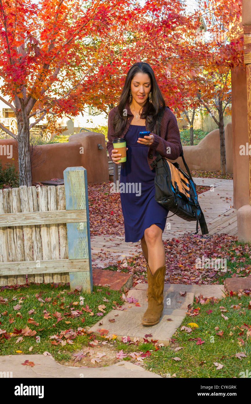 Hispanic woman carrying coffee and text messaging on cell phone Stock ...