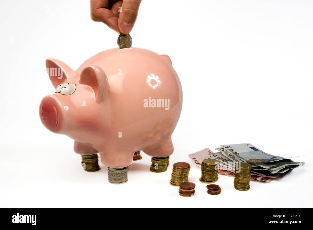 A hand is putting a 2 euro coin into a saving pig Stock Photo