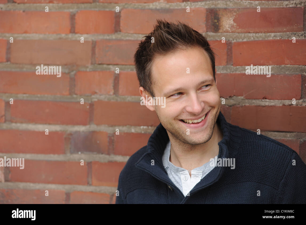 Smiling man leaning against brick wall Stock Photo - Alamy