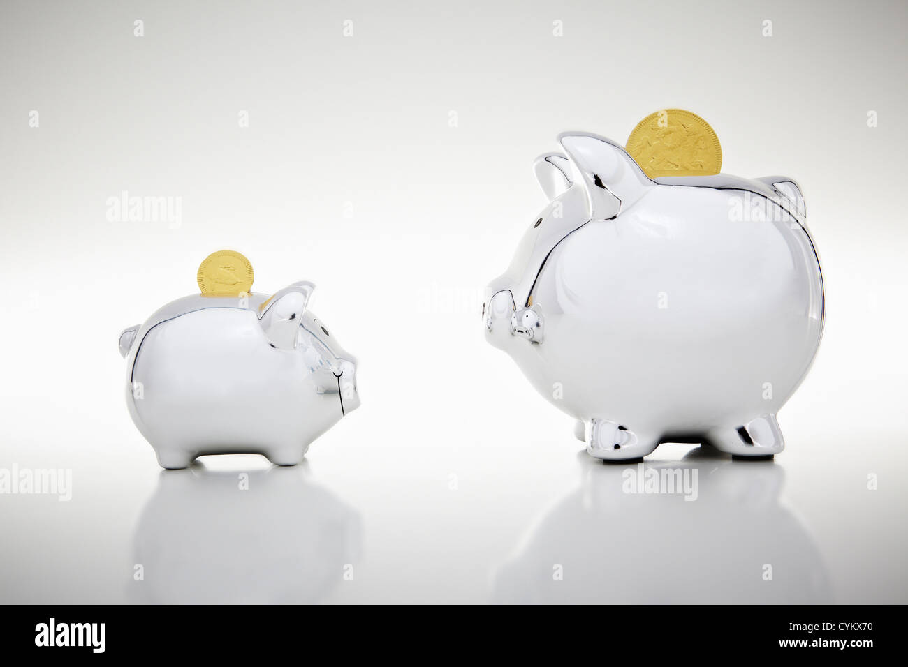 Gold coins dropping into piggy banks Stock Photo