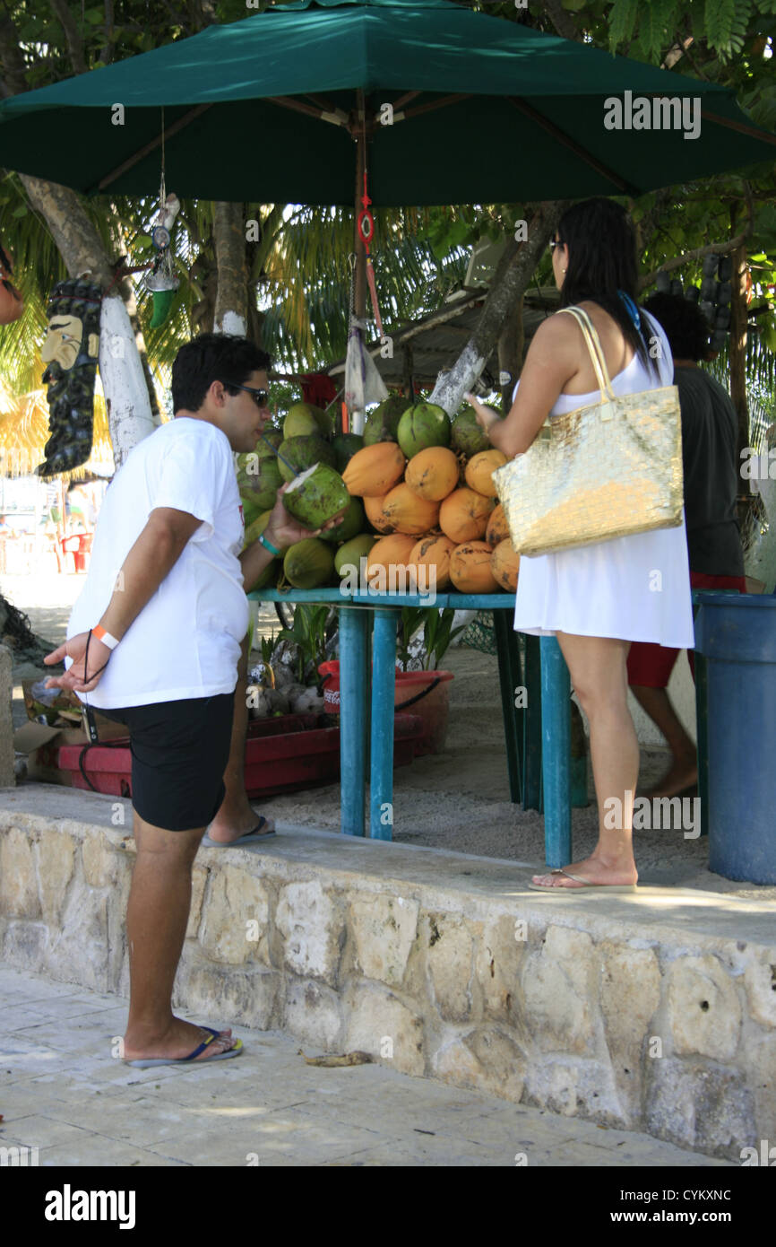 A couple on holiday buying fresh coconut drinks from a street vendor, Isla Mujeres, Mexico Stock Photo