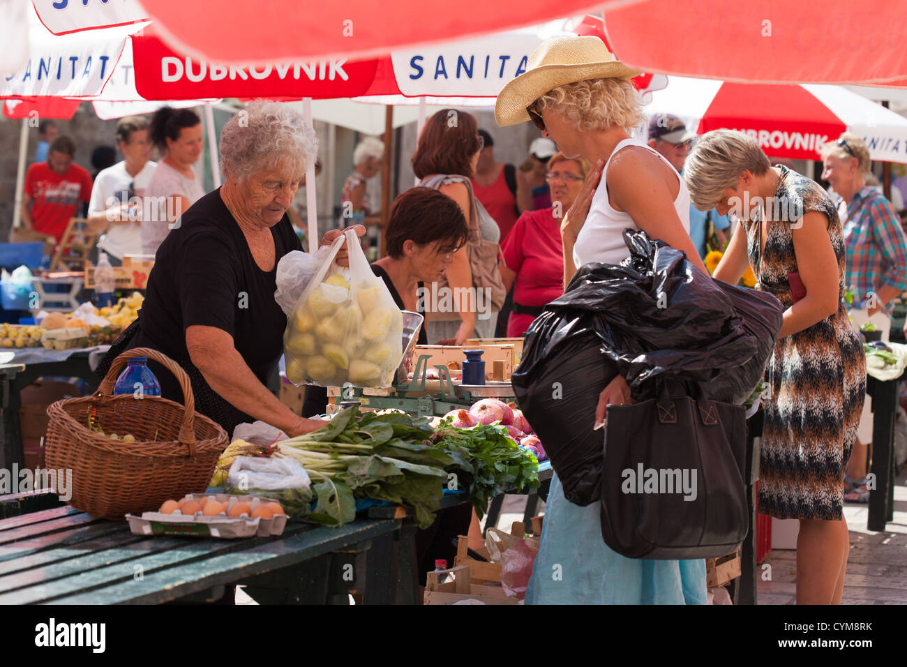 Older woman, market stall holder and shoppers in Dubrovnik city market. Croatia Stock Photo