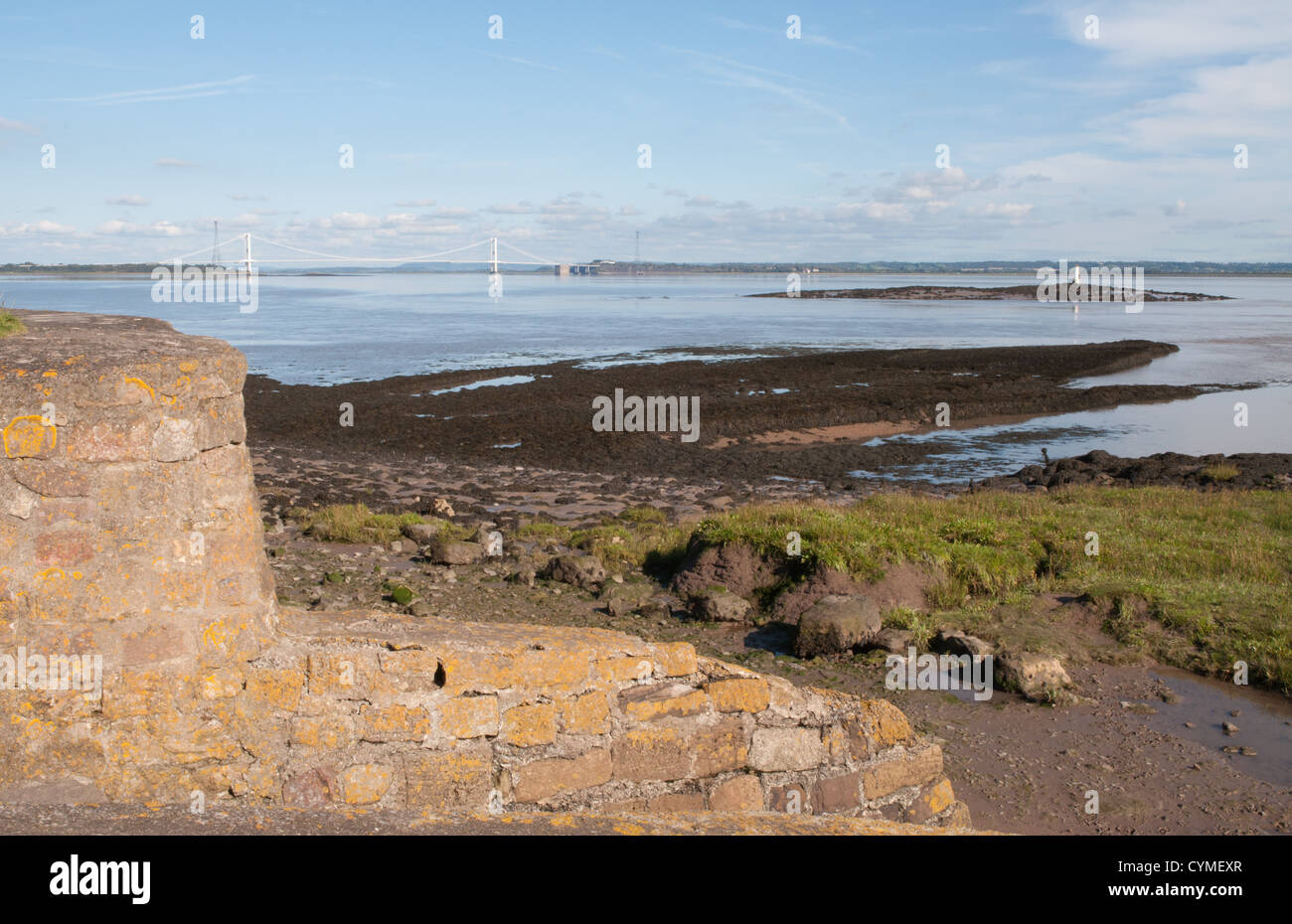 river estuary low tide rocks sunlit stone wall and structure blue sky white clouds sunny Stock Photo