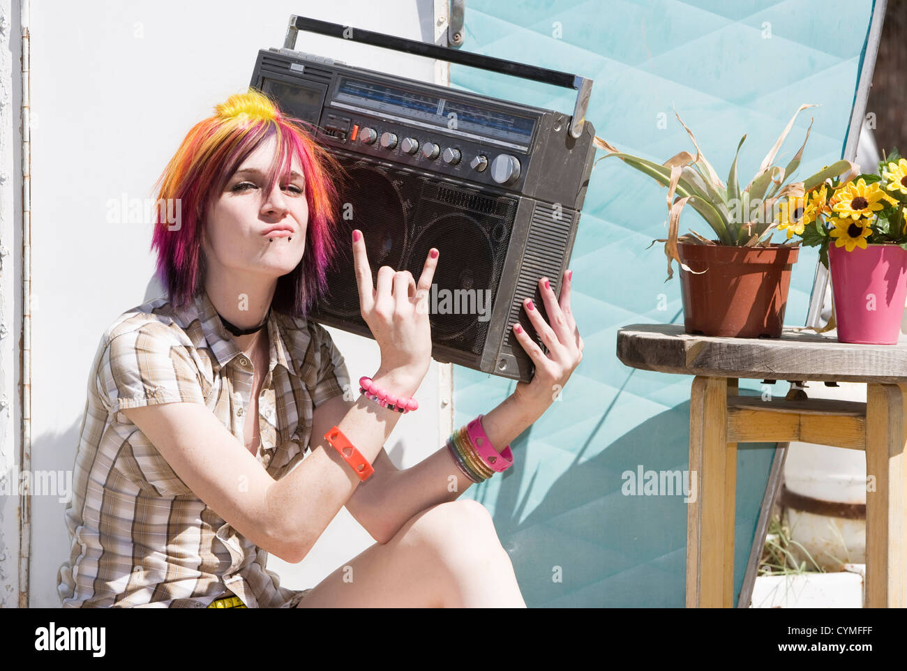 Punk girl with brightly colored hair sitting on trailer step holding boom box Stock Photo