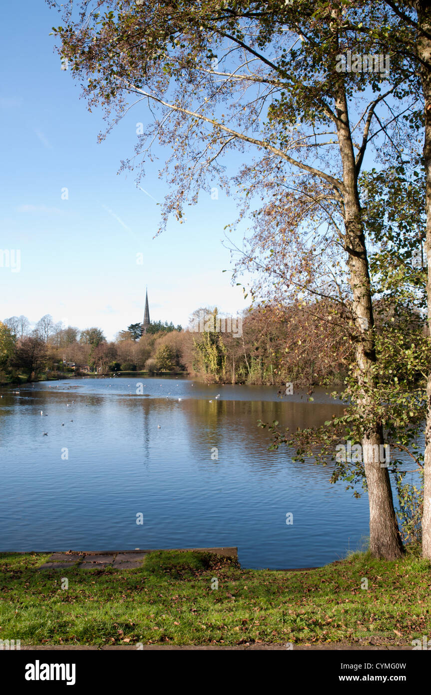 small lake. calm, reflections, blue sky, tree foreground, church with spire in background, sunny Stock Photo