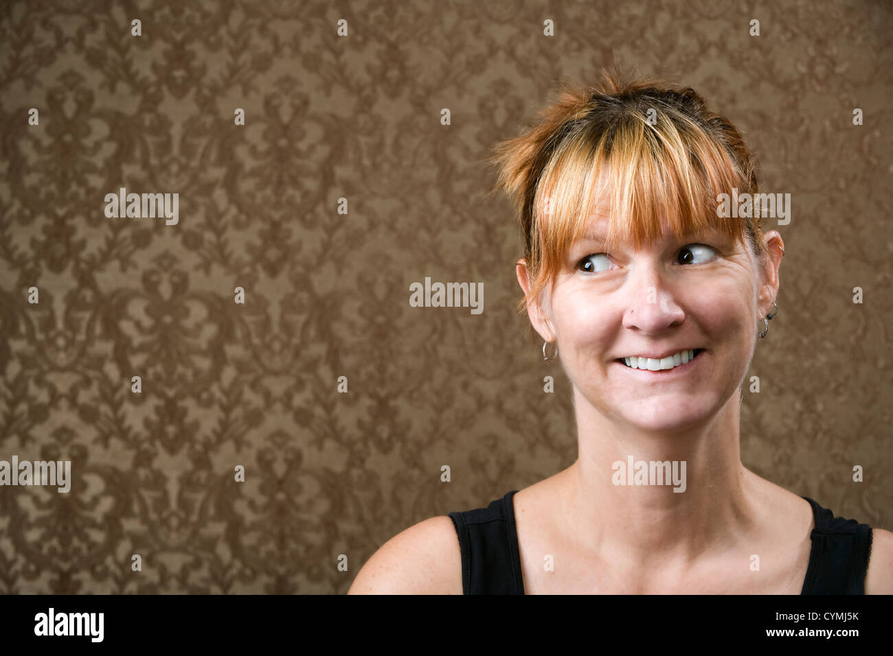Pretty woman smiling in front of a gold-flocked wallpaper background Stock Photo