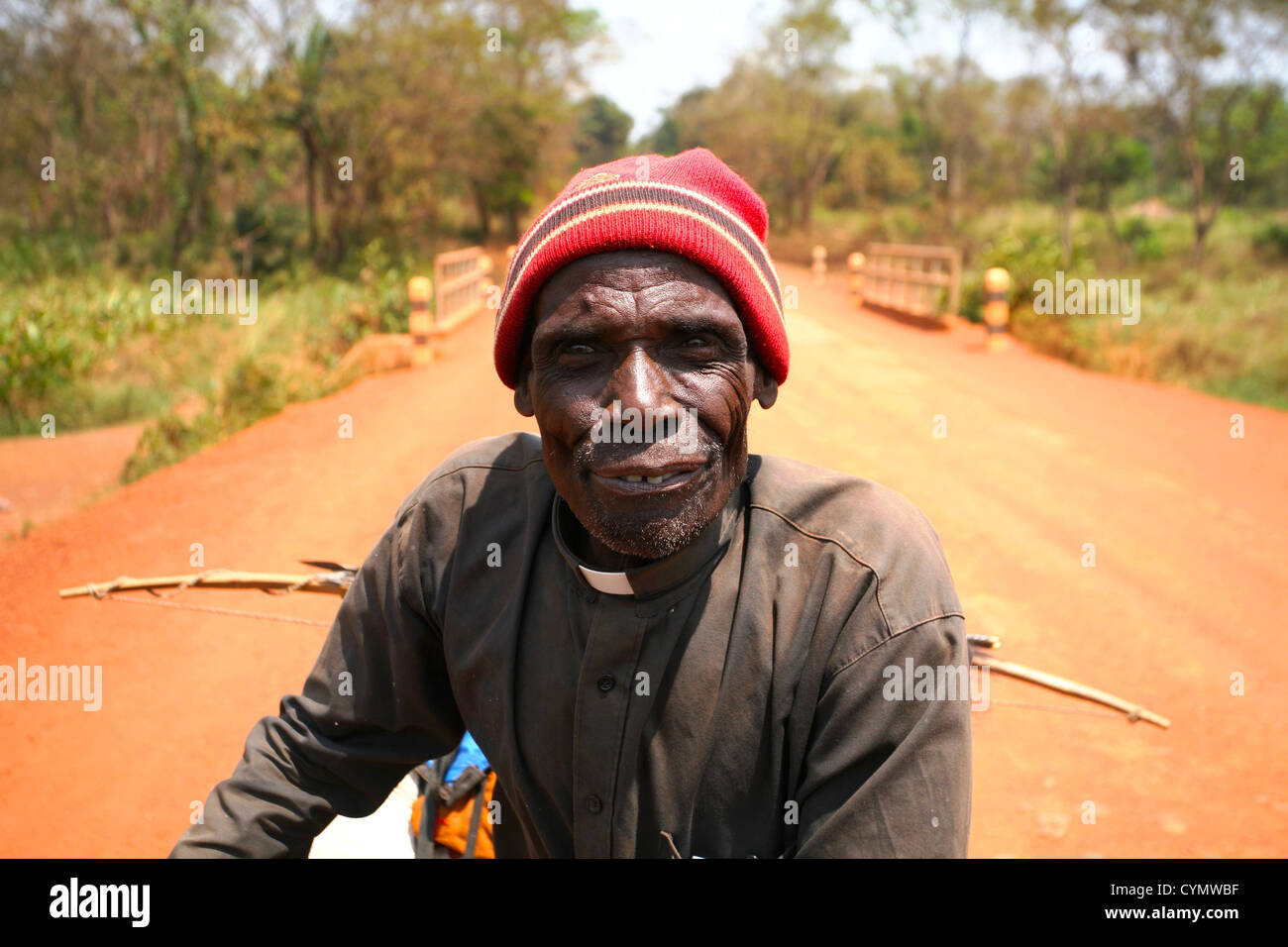 Unidentified Priest with Bow & Arrow  on back of bike near Yambio, Western Equatoria, South Sudan in late 2010 Stock Photo