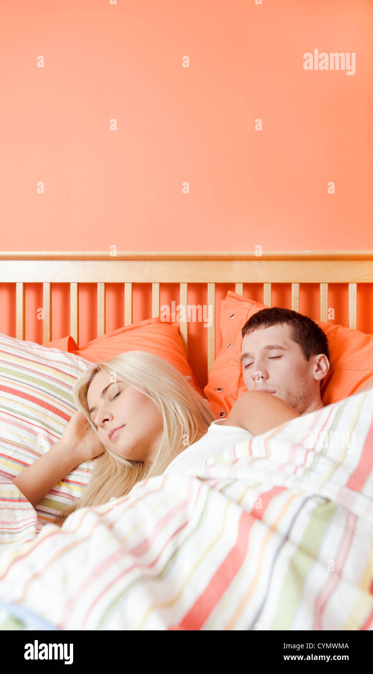 Young couple sleep closely together under a striped bedspread. Vertical