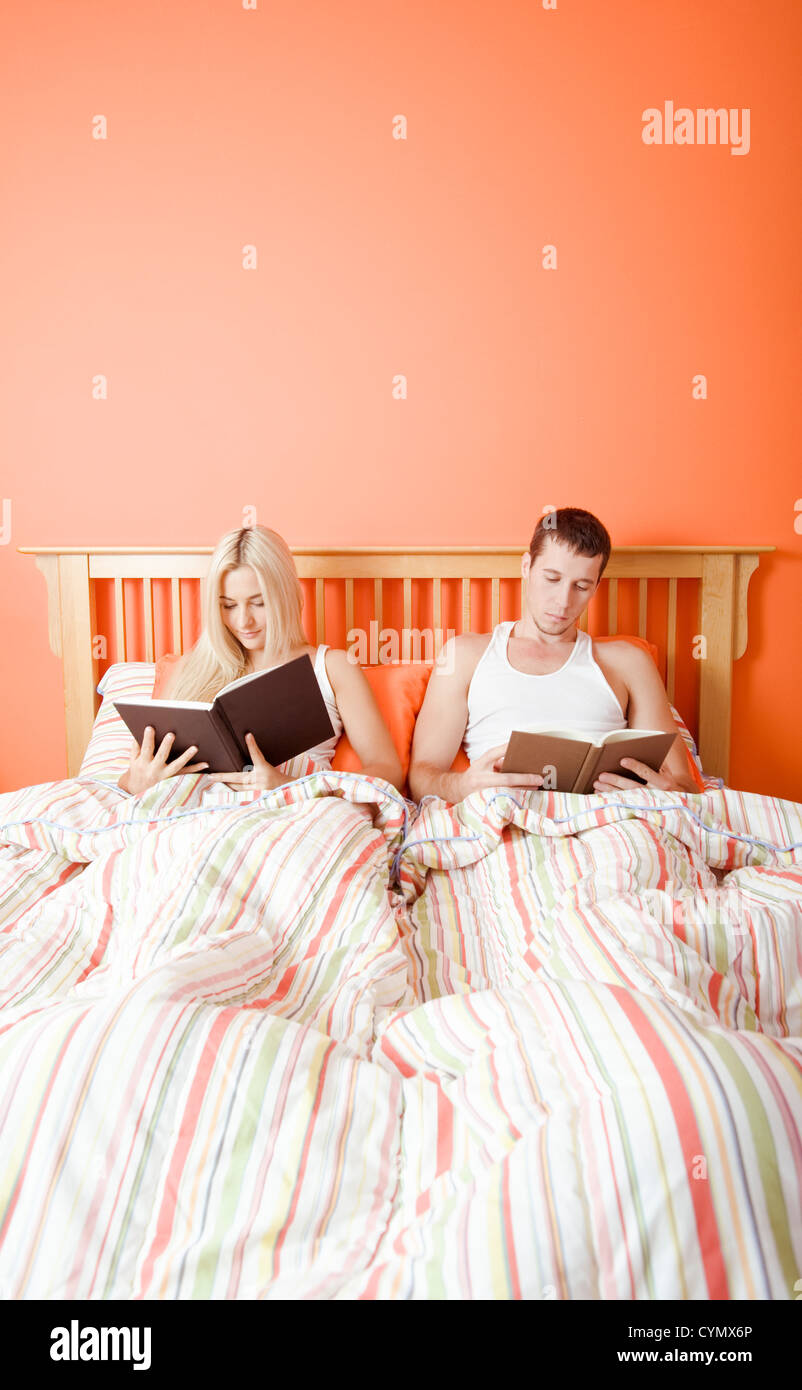Man and woman reading side-by-side in bed. Vertical format. Stock Photo