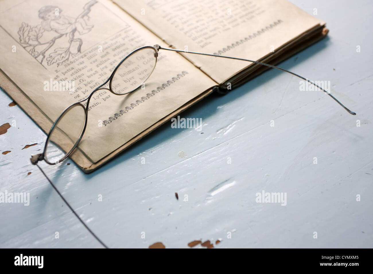 old fashioned reading glasses on top of an old book on a table Stock