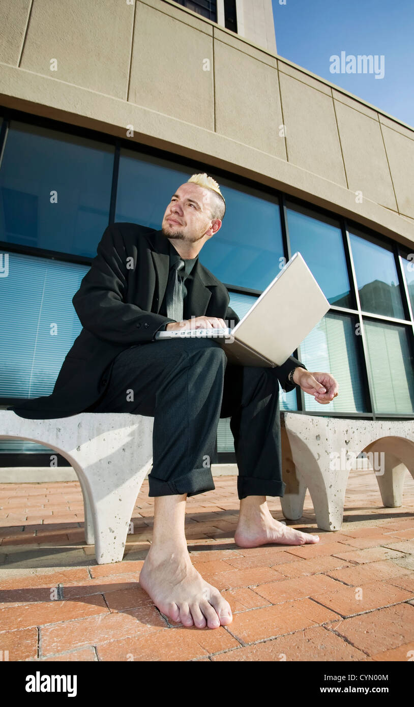 Barefoot businessman with a punk haircut works on his laptop computer ...