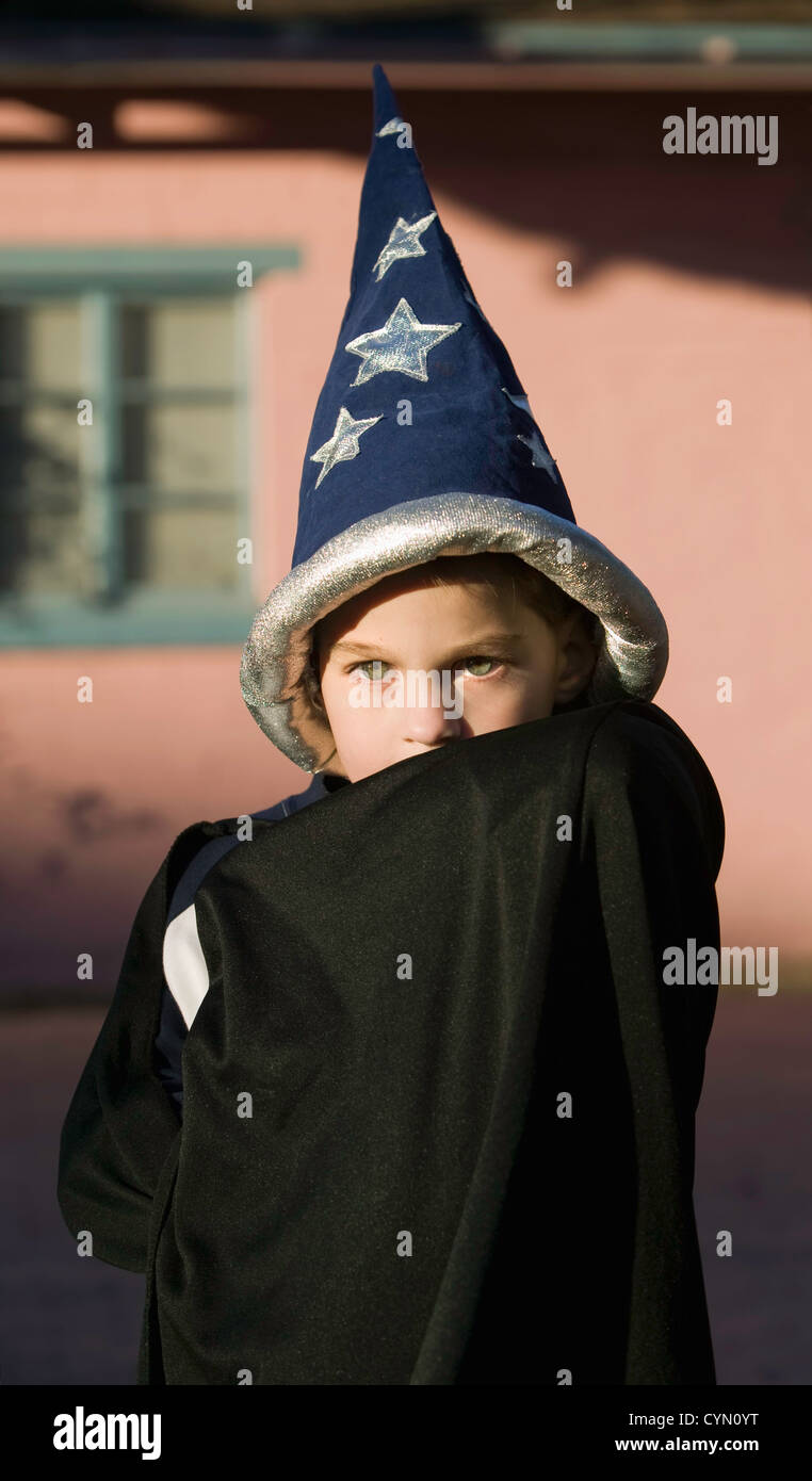 Youn boy with a wizard hiding his face in front of a pink house Stock Photo