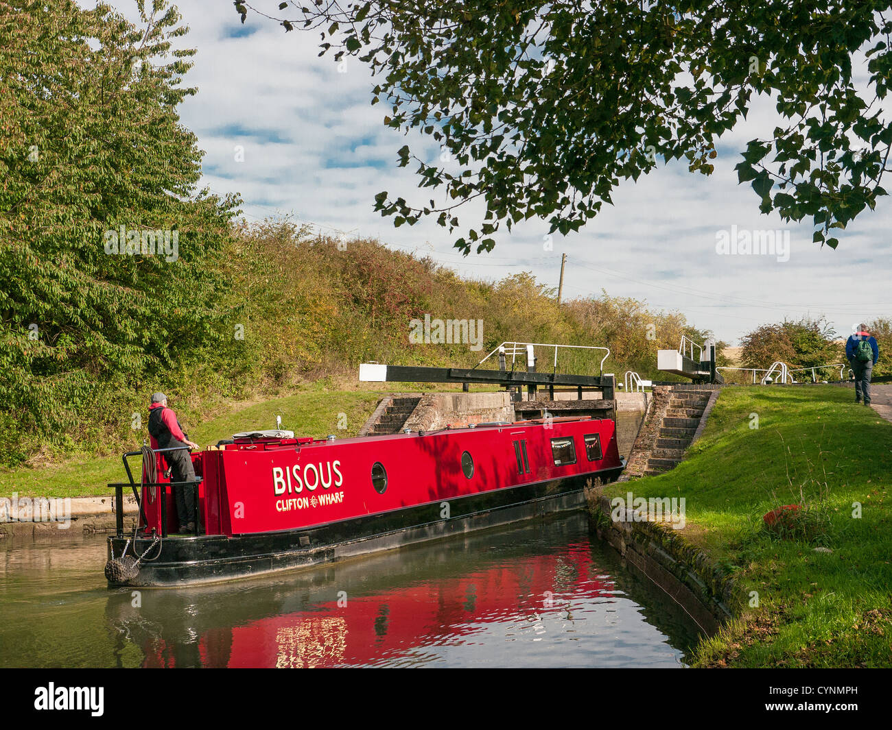 Red Narrowboat coming out of a lock and lockeeper on the Grand Union Canal at Marsworth, Buckinghamshire, UK Stock Photo
