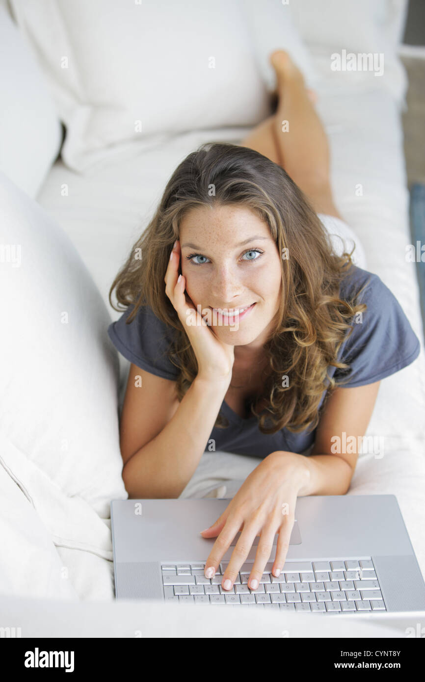 Beautiful young woman lying on sofa with laptop Stock Photo - Alamy