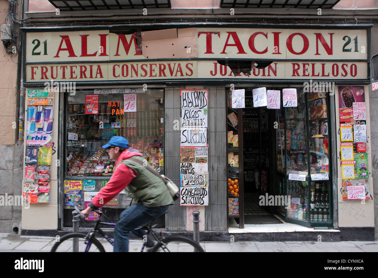 Male cyclist passes Alimentacion food drink grocery shop, Madrid, Spain Stock Photo