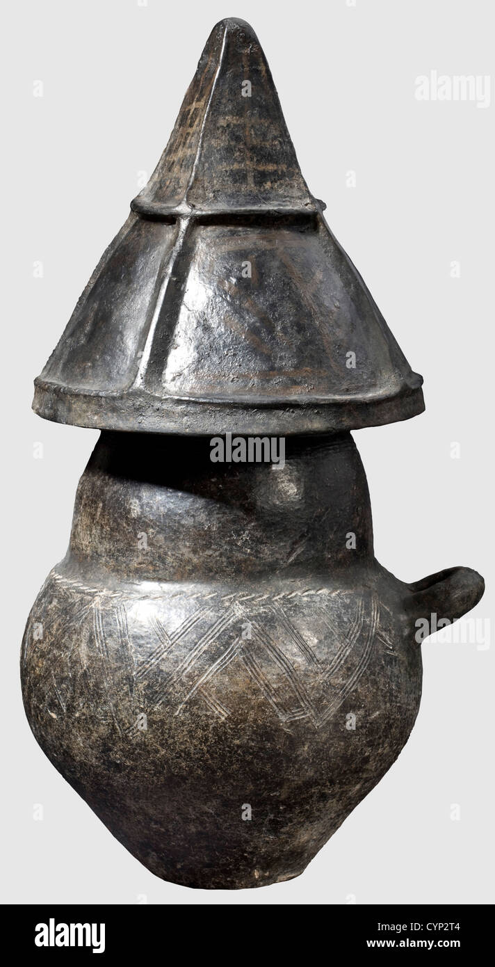 A cinerary urn with pointed helmet lid,Villanova,9th/8th century B.C.Dark brown to black earthenware.Single handle,biconical urn with a flaring rim and graffito decoration with white incrustation.The upper part of the urn with a continuous band of meander.The lid in form of a pointed helmet sectioned by four sturdy vertical ribs and one horizintal rib.The sections decorated with painted geometrical patterns.The horizontal rib pierced.Heigth of the urn 33.5 cm,heigth of the lid 24.5 cm.Smaller restorations and additions.Axel Guttmann Collection(wit,Additional-Rights-Clearences-Not Available Stock Photo
