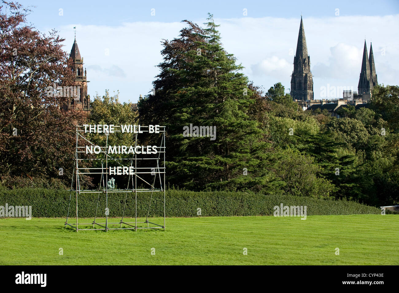 : A 'No Miracles Here' sign in the gardens of The Scottish National Gallery of Modern Art in Edinburgh, Scotland with three church spires in the City behind. It is is an installation by Scottish artist Nathan Coley. Stock Photo