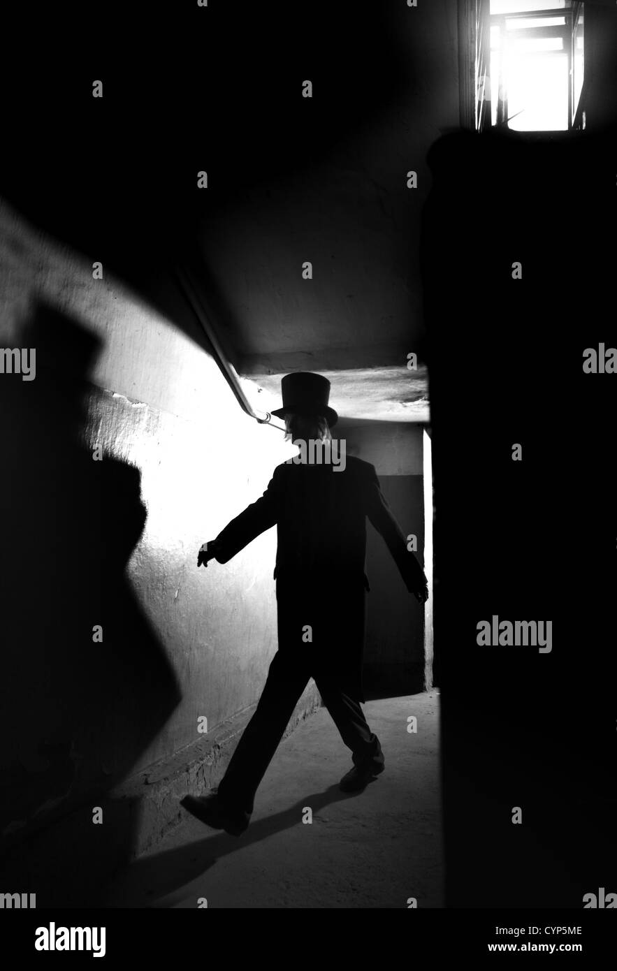 Silhouette of the man in black coat and hat going in the dark interior Stock Photo