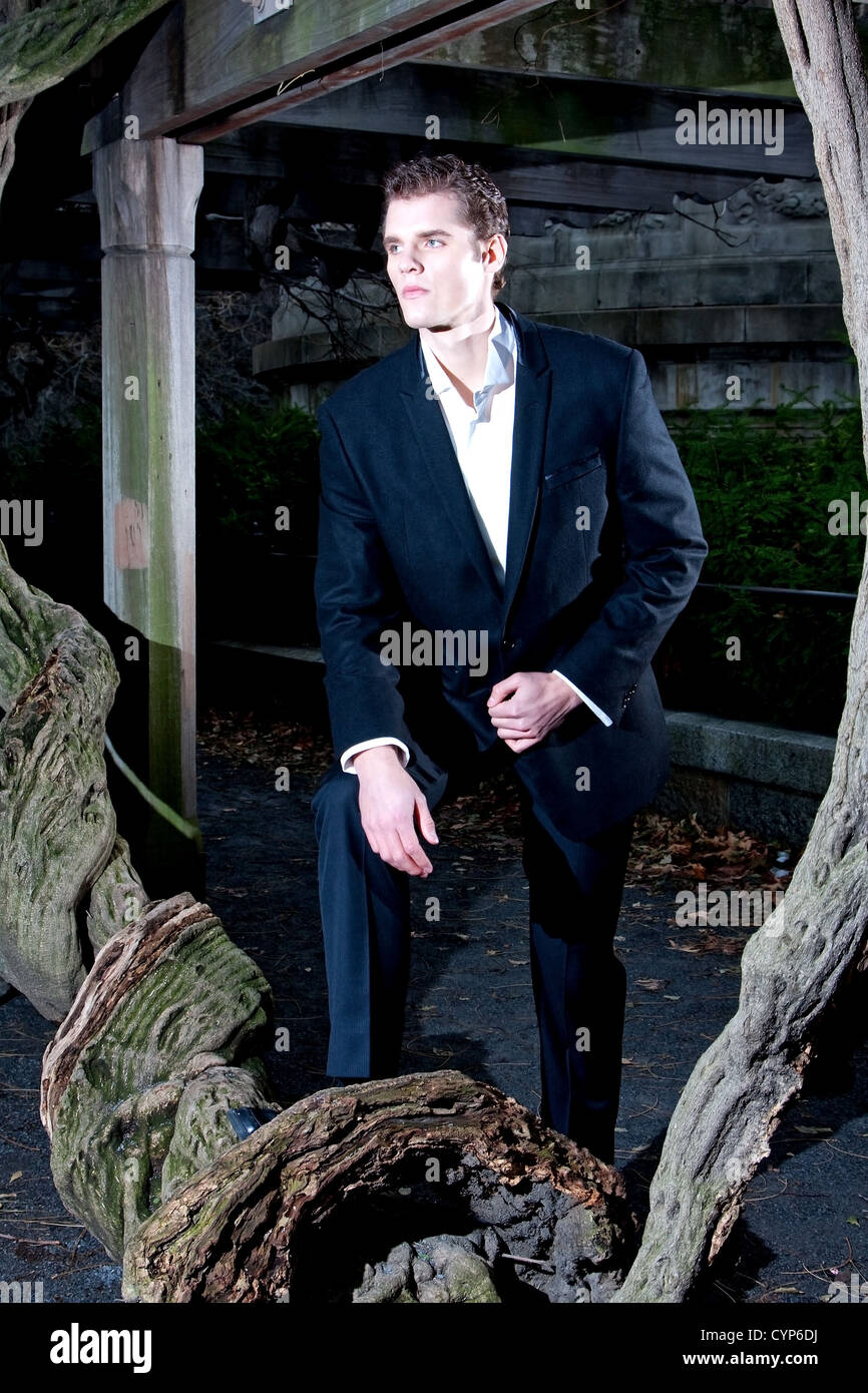 Handsome Caucasian guy having his foot on a vine tree under a pergola at night Stock Photo