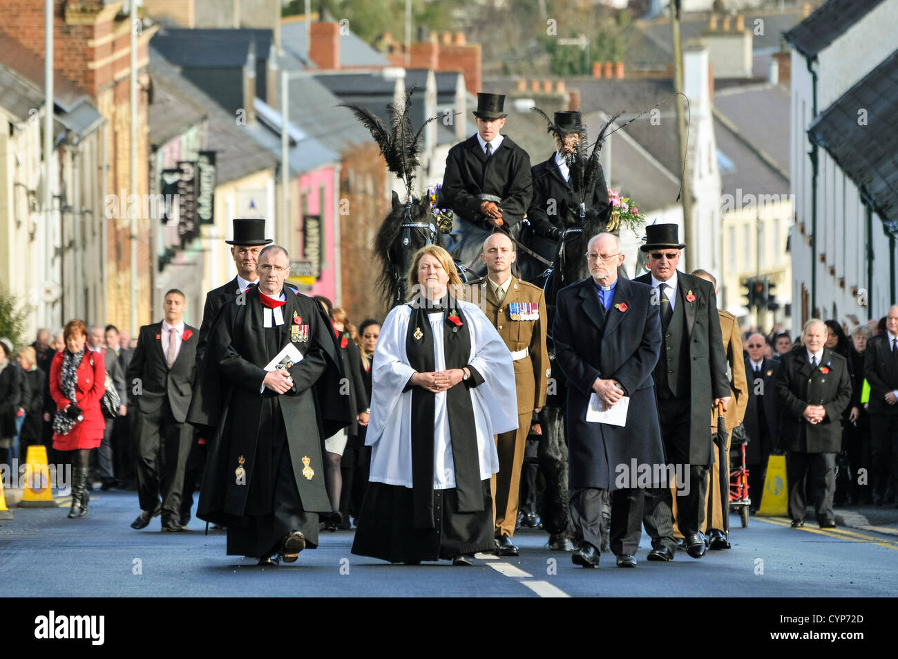 A funeral procession with a horsedrawn hearse makes its way up a steep