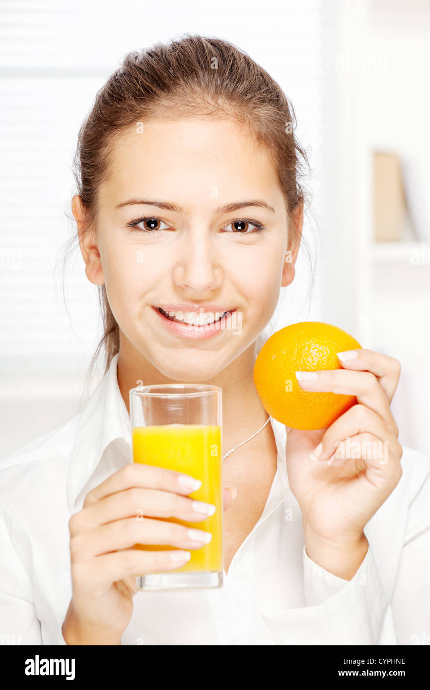 Young smiling woman holding glass of juice and orange at home Stock Photo