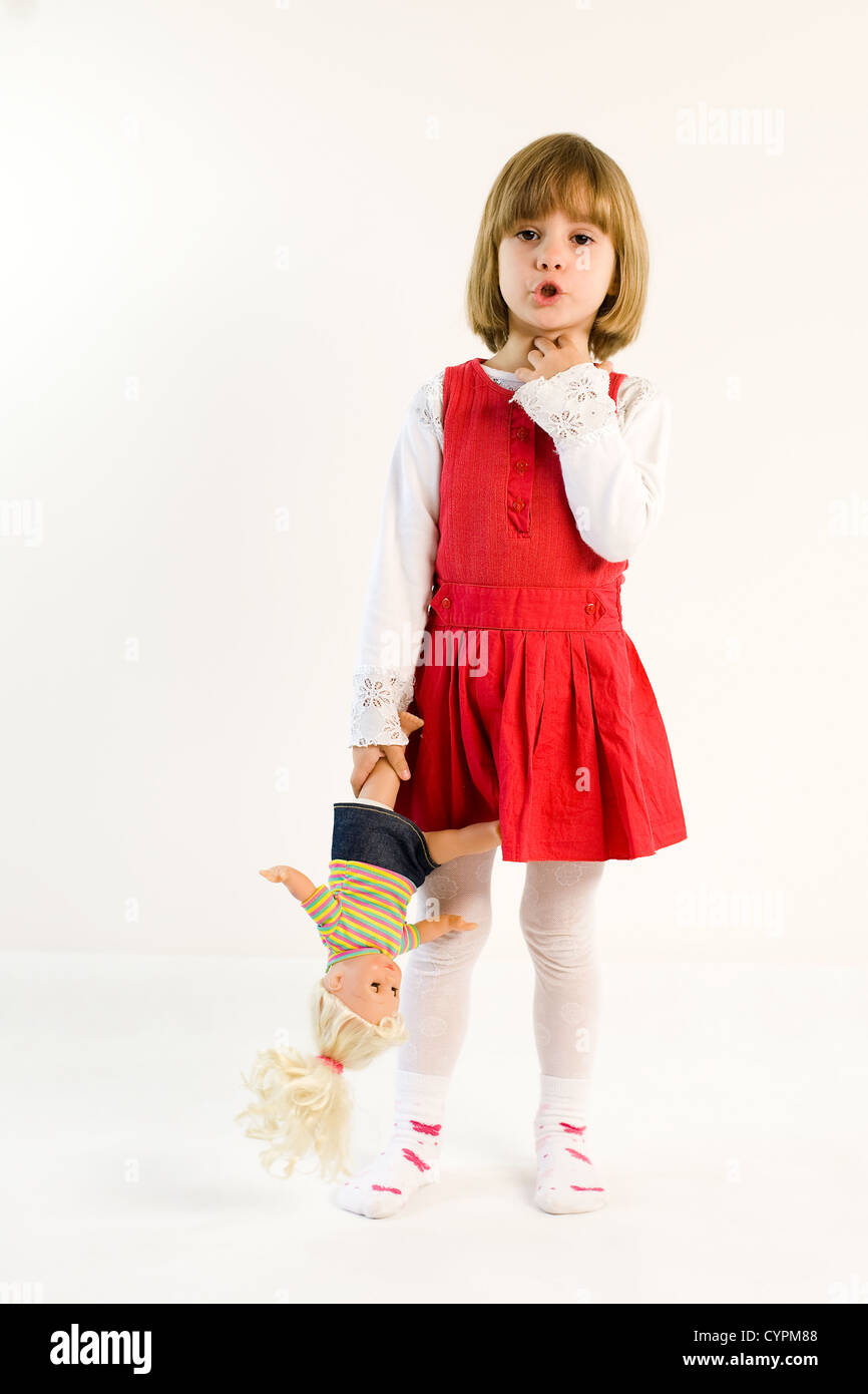 Little girl in a red dress is talking and holding doll upside down Stock Photo