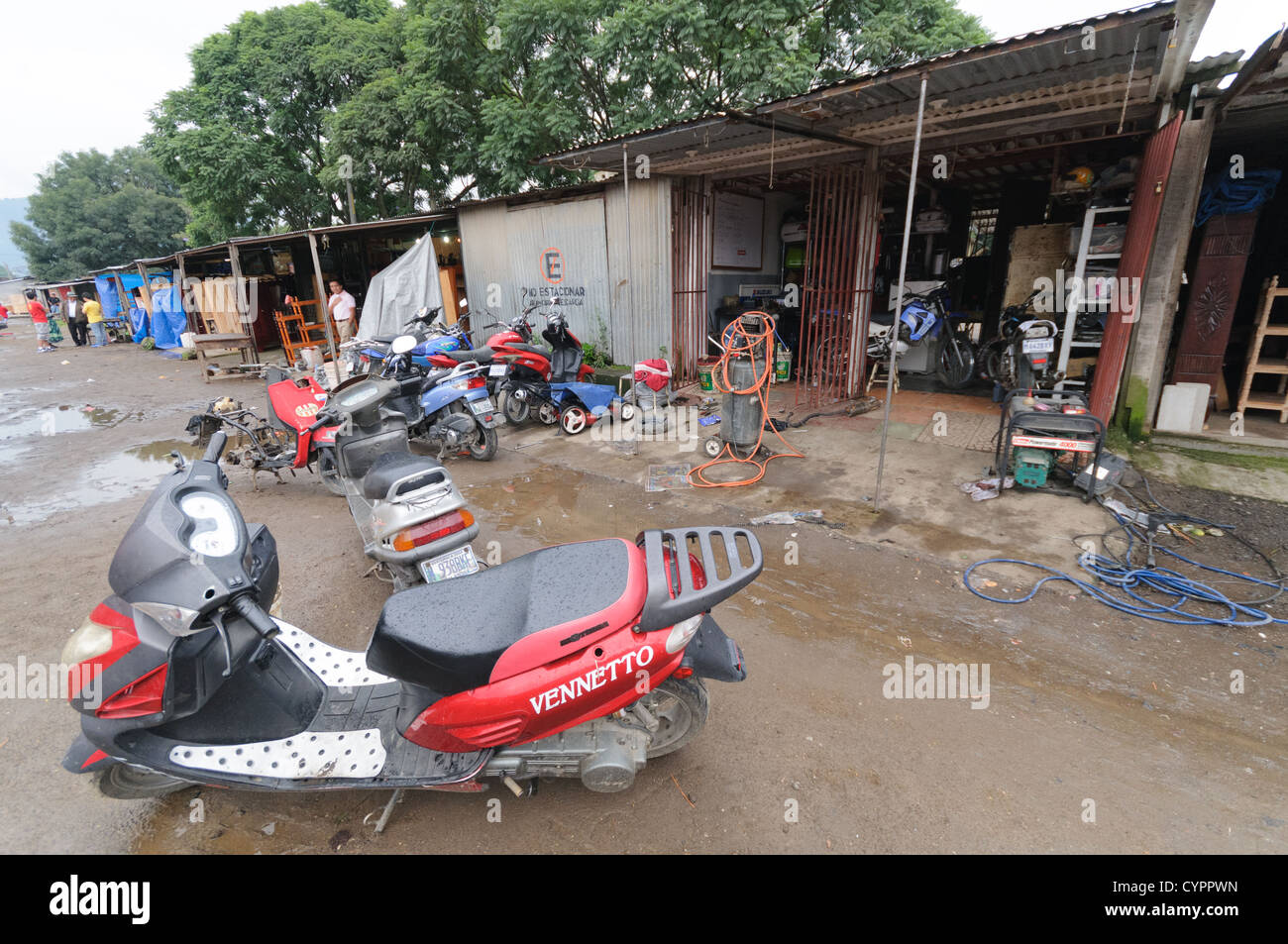 Scooter repair shop behind the Mercado Municipal (town market) in Antigua, Guatemala. From this extensive central bus interchange the routes radiate out across Guatemala. Often brightly painted, the chicken buses are retrofitted American school buses and provide a cheap mode of transport throughout the country. Stock Photo