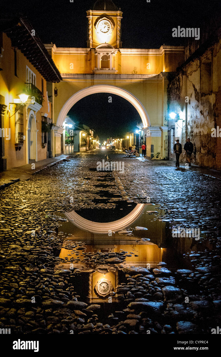 The archway over the street of the convent of Santa Catalina in central Antigua, Guatemala, with the water from recent rain reflecting the lights on the cobblestone street. Stock Photo