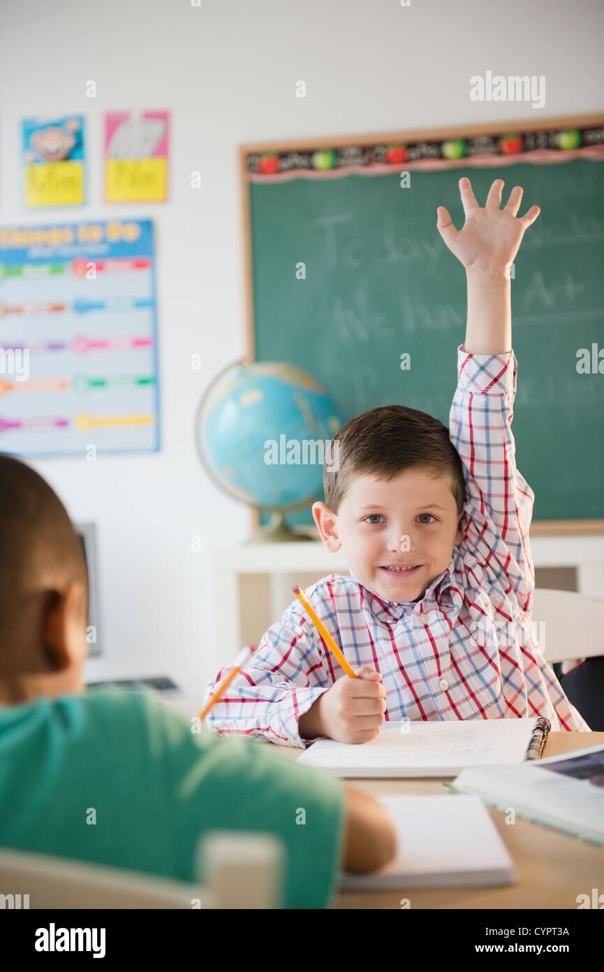 Caucasian boy raising hand in classroom Stock Photo