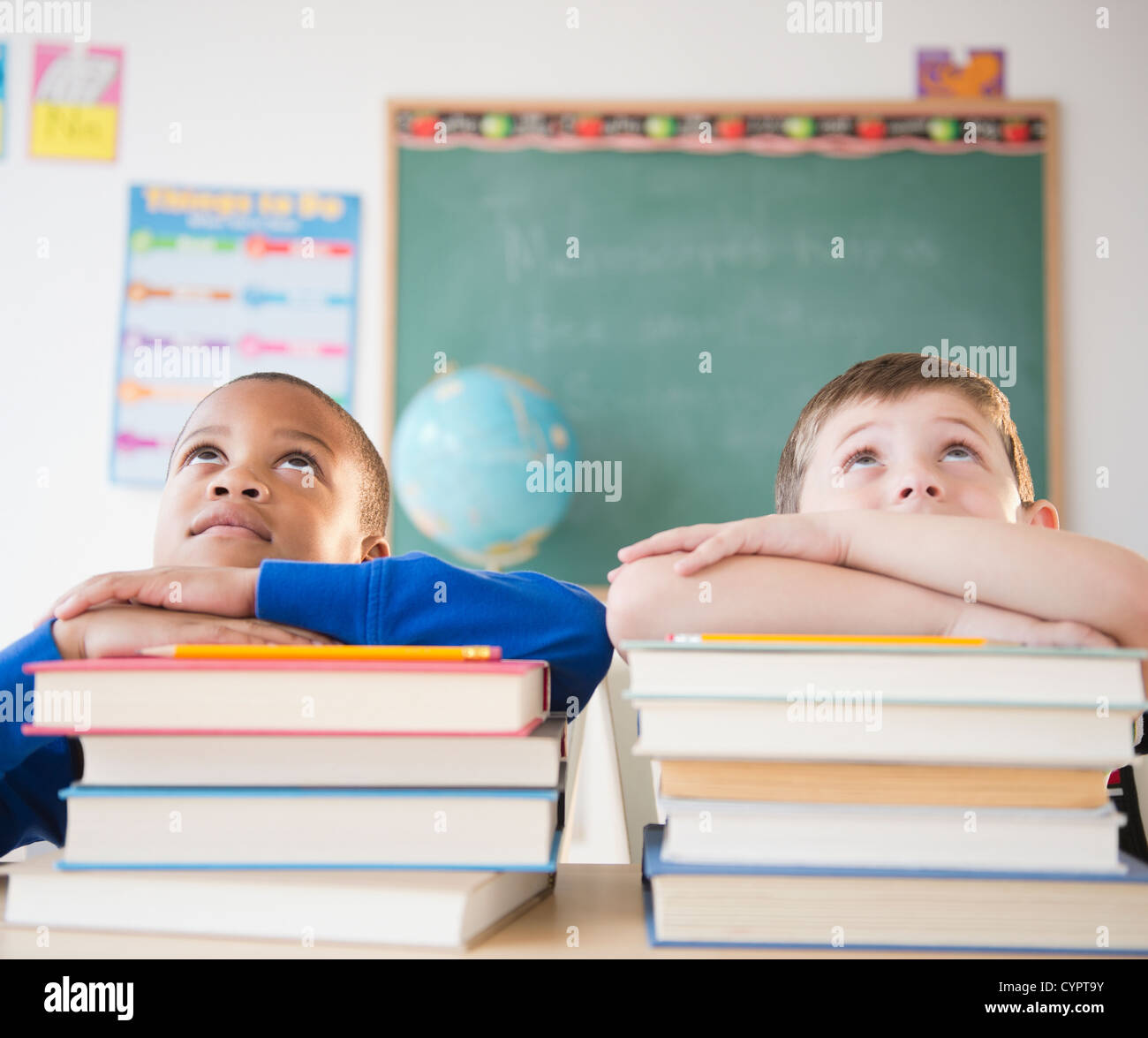 Students leaning on stacks of books in classroom Stock Photo