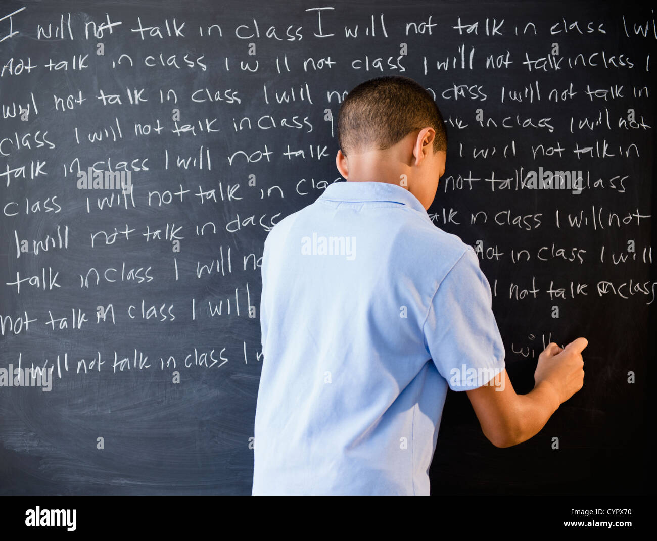 Hispanic boy writing punishment on blackboard Stock Photo