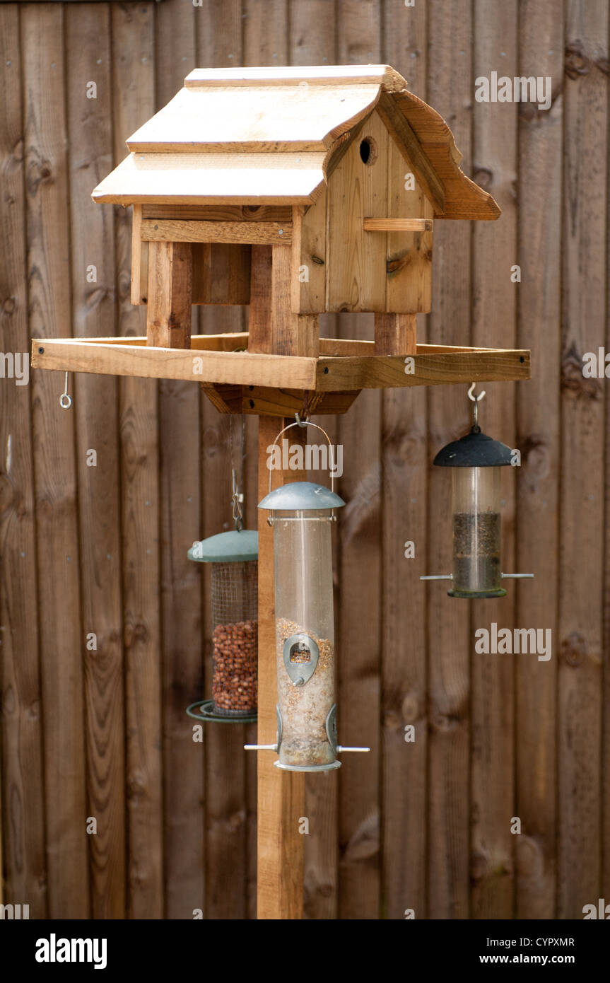 Wooden Bird Feeder Against A Wooden Fence With Nut Filled Feeders