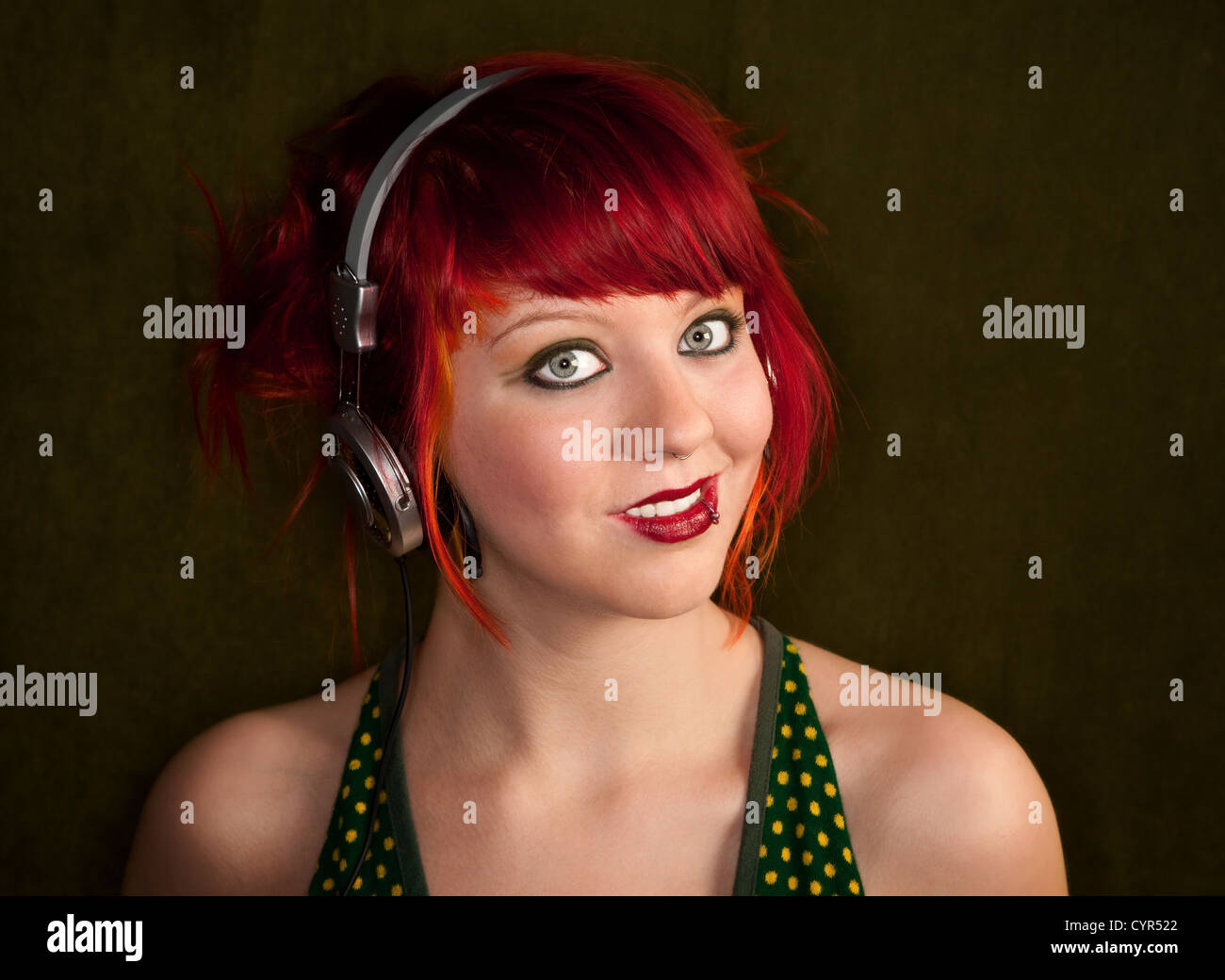Pretty punky girl with brightly dyed red hair listening to music Stock Photo