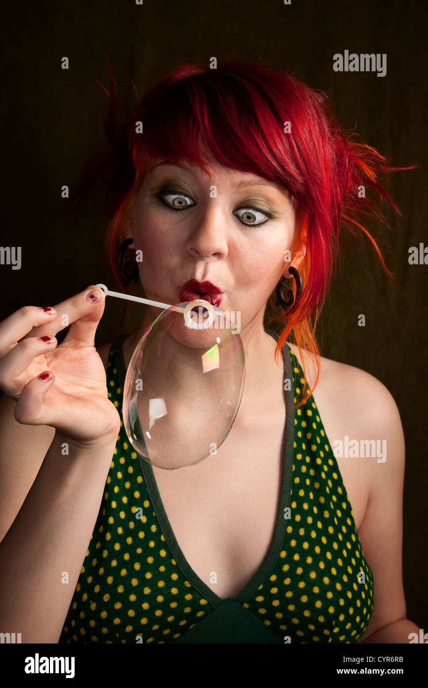 Pretty punky girl with brightly dyed red hair trying to blow a bubble Stock Photo