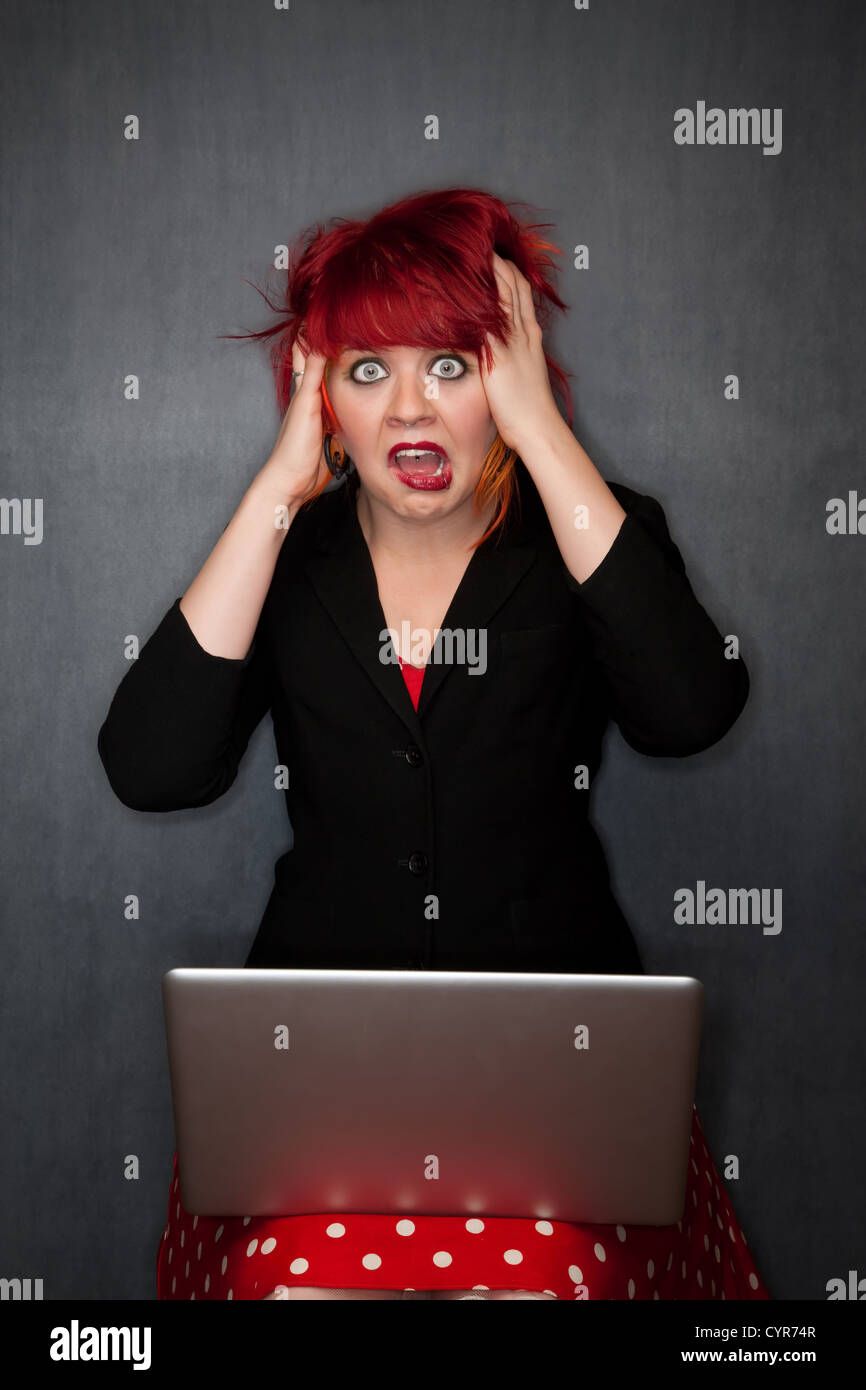 Pretty punky girl with brightly dyed red hair with laptop computer Stock Photo