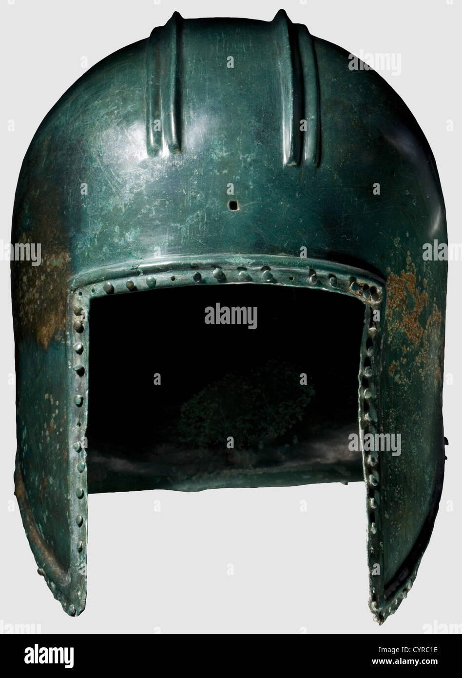 An Illyrian type helmet,6th century B.C.Bronze with fine green noble patina.Of domed form,the crown with two raised parallel ridges extending from front to back forming a crest base.A rectangular hole pierced at centre front for crest attachment.Rectangular face opening,the pointed cheekpieces with pierced holes for the chinstrap.Slightly flaring neck-guard.The edge bordered by a moulded rib and a row of pierced holes for lining attachment with partially preserved rivets.Small corrosion pits in some places,slightly torn at rear.Height 22 cm.Good me,Additional-Rights-Clearences-Not Available Stock Photo