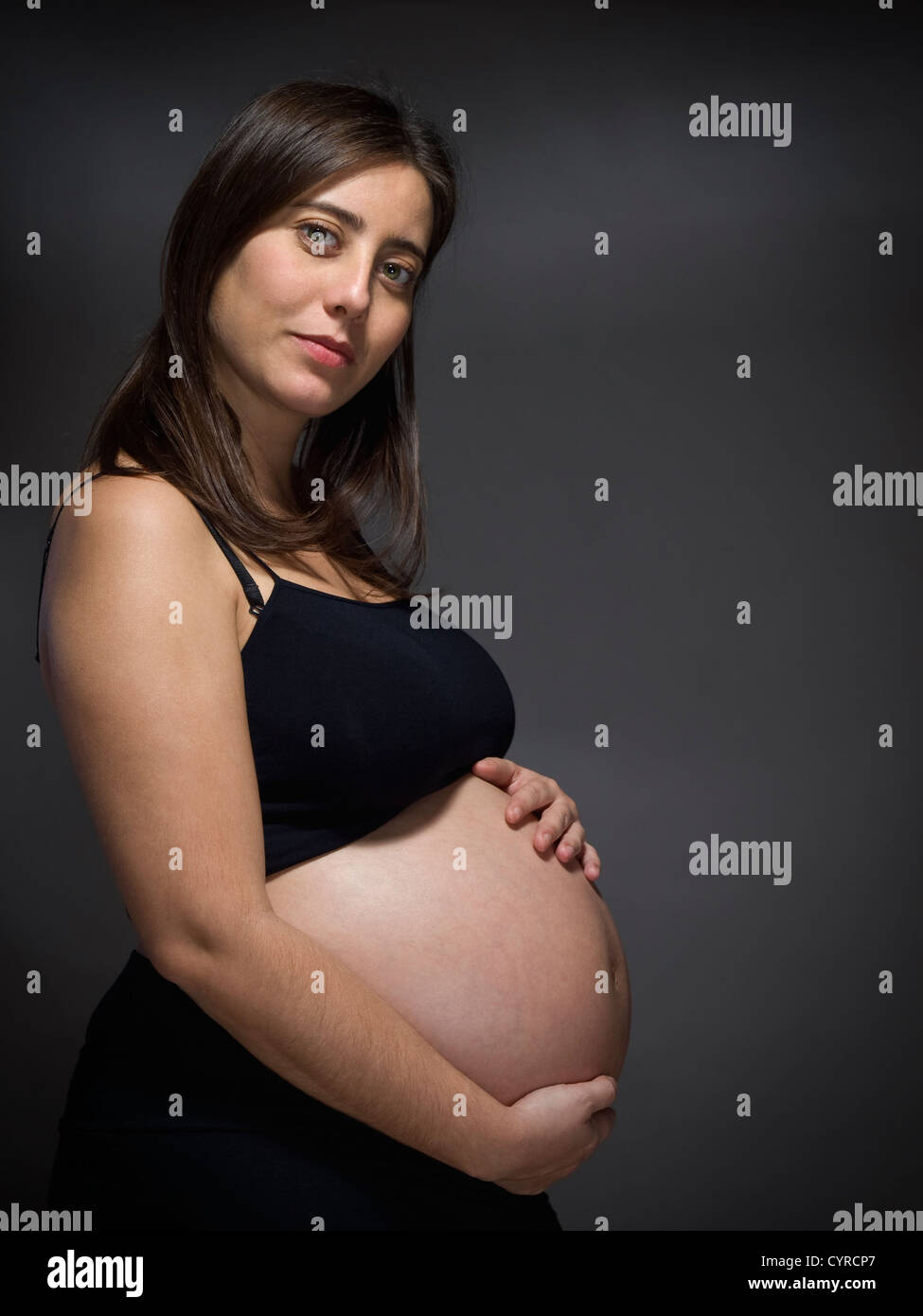 A pregnant woman holds her big belly over a gray background Stock Photo ...