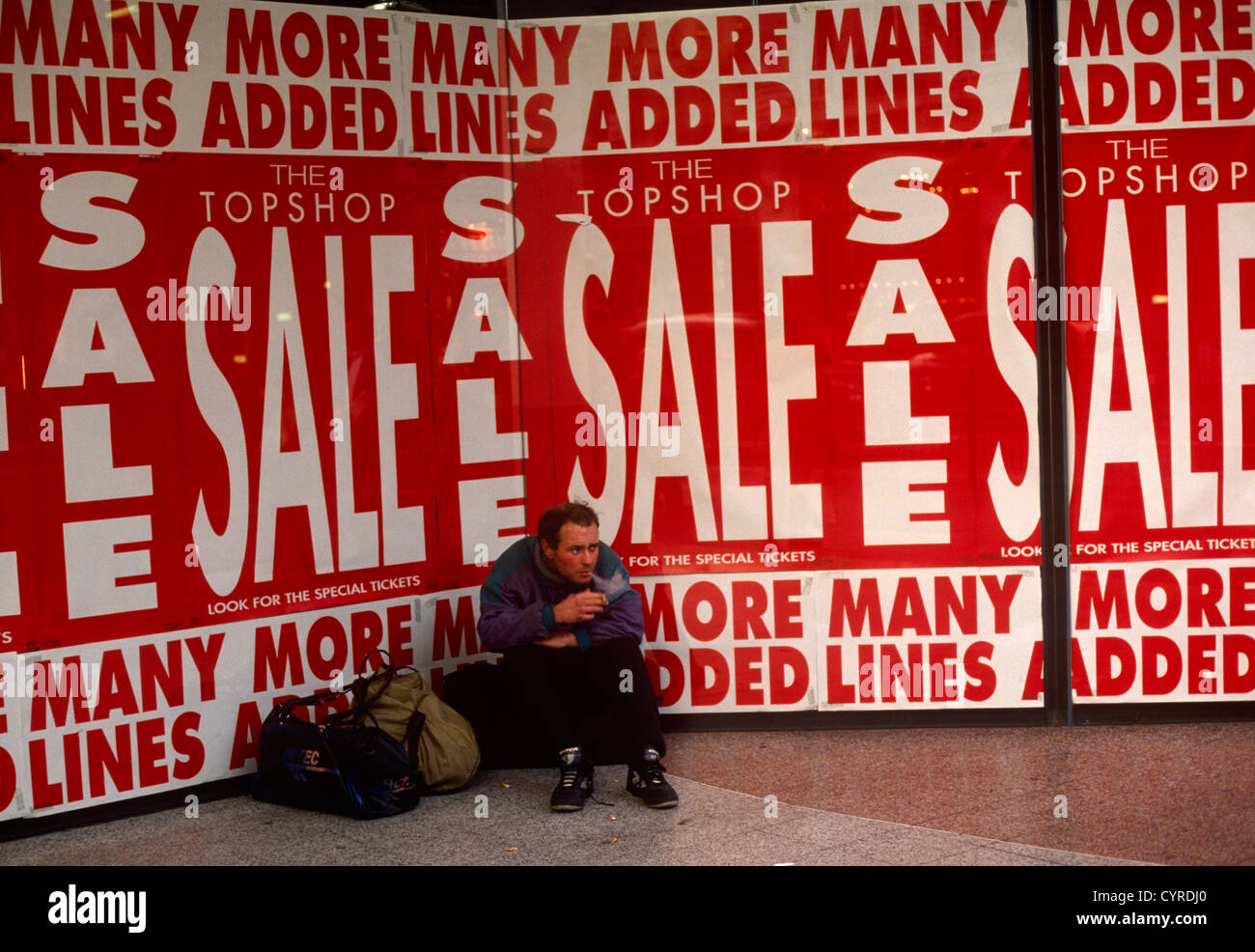 Beneath retail Sale posters, a young man rests in the front of a London ...