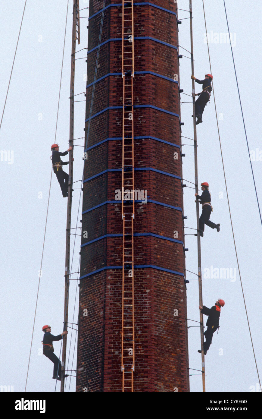 Young apprentices climb ladders to the top of a tall chimney during a