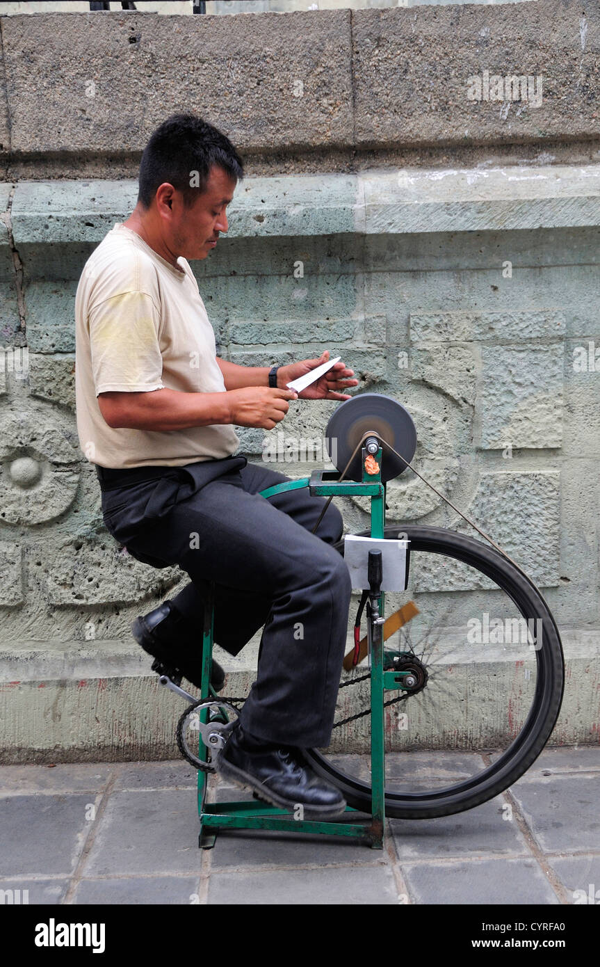 Mexico, Oaxaca, Traveling knife sharpener in the Zocalo. Bicycle foot pedal operated machine set up on a pavement sidewalk. Stock Photo