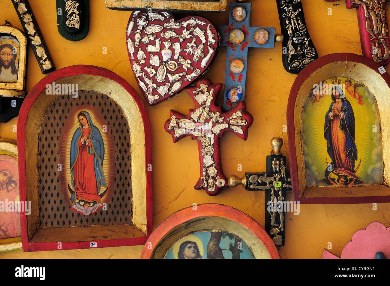 Religious kitsch art displayed on yellow painted wall  American  Hispanic Latin America Latino Mexican Religion Shops Shoppers Stock Photo