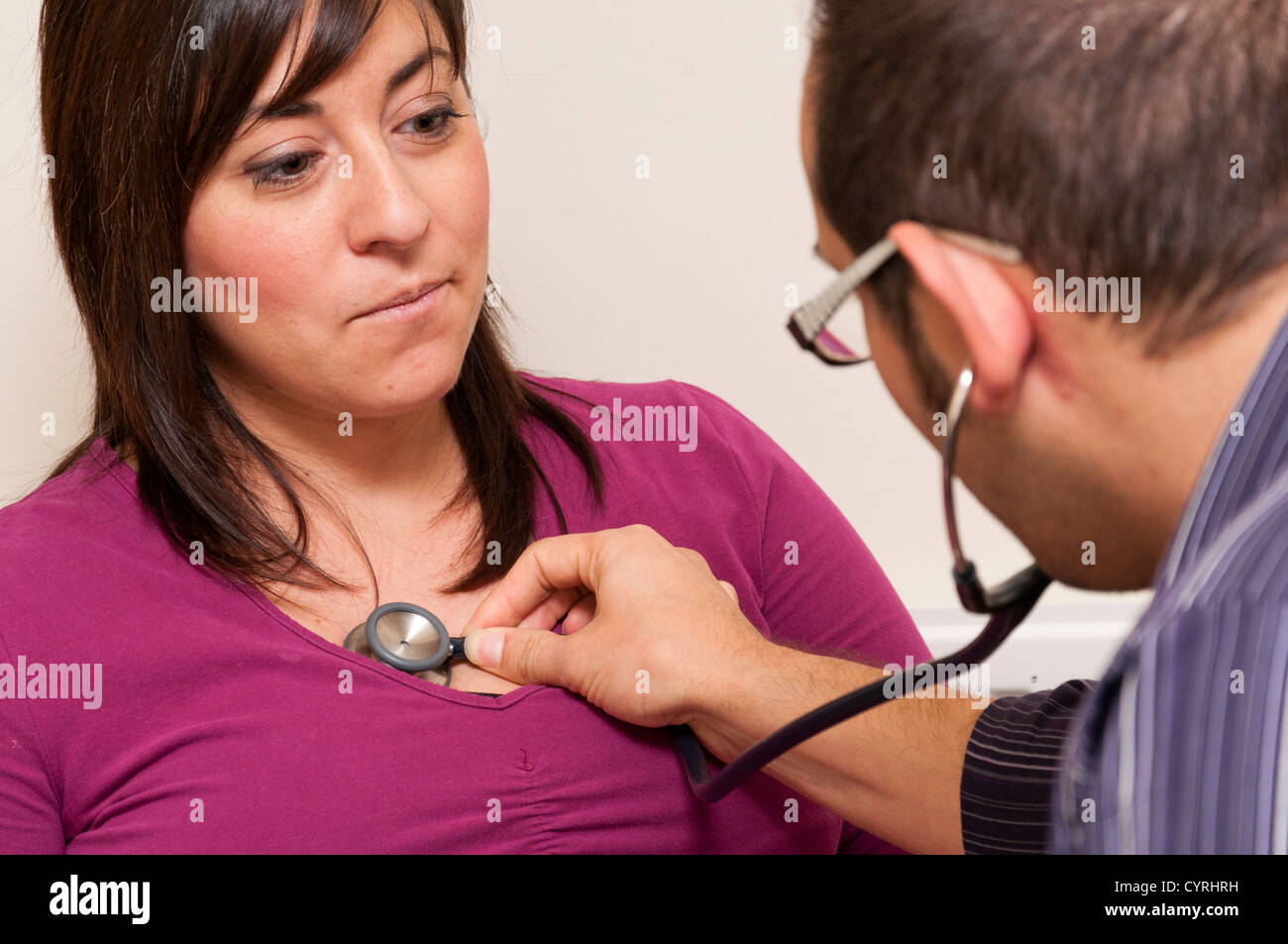 GP Doctor surgery patient consultation UK. Doctor listening to patient heart using stethoscope. Stock Photo